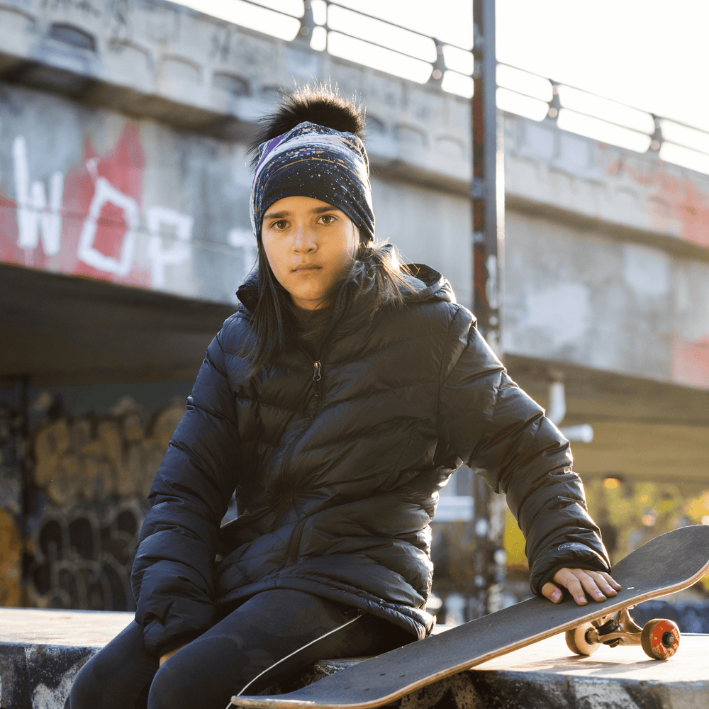 Young girl wearing the Abracadabra beanie and black jacket sits with a skateboard