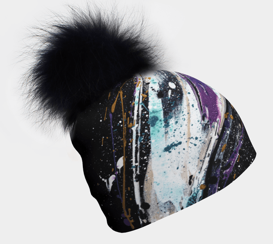 Black beanie with abstract colorful paint splatters and a large fluffy black pompom