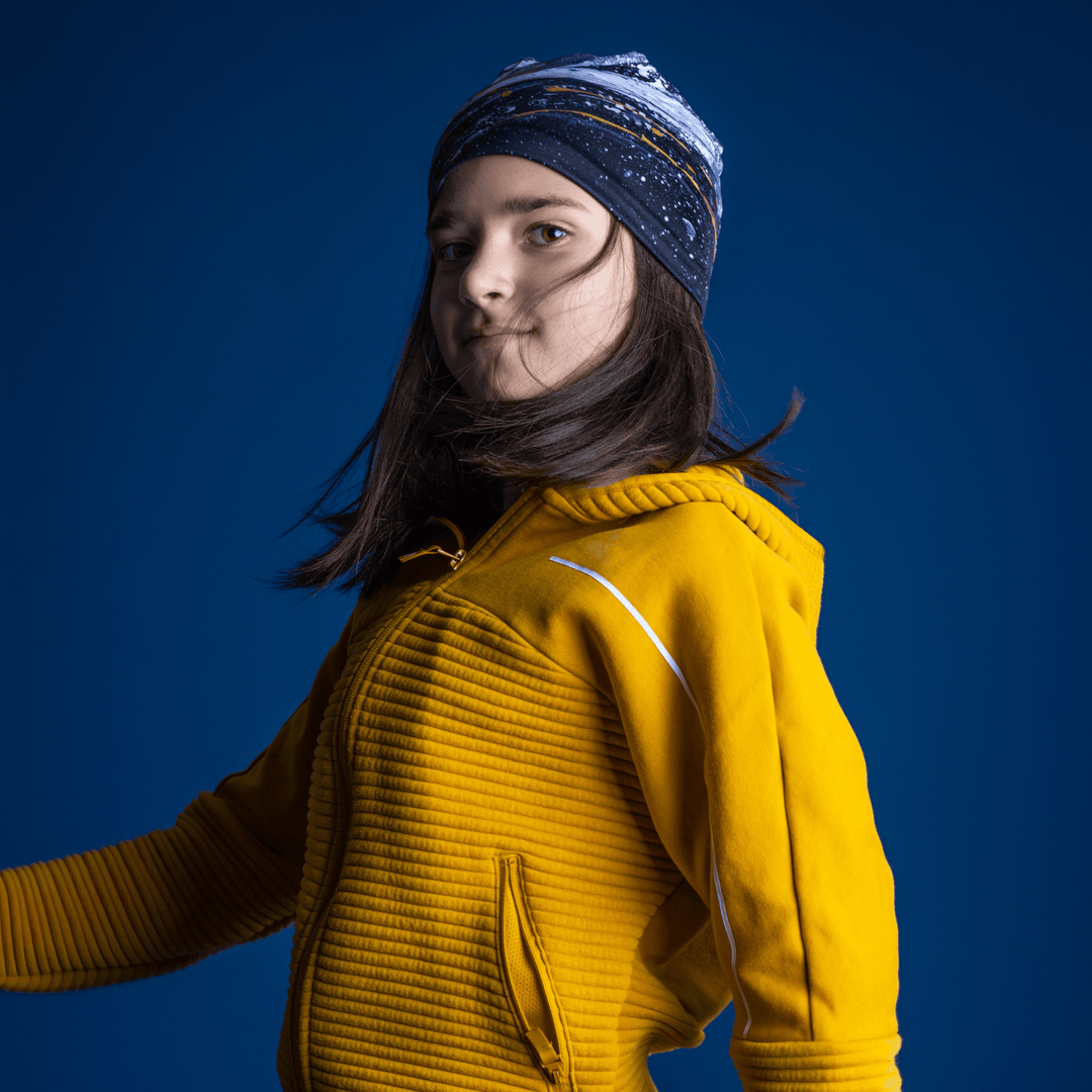 Young girl in a yellow jacket, dynamically turned, wearing the Abracadabra Beanie as a headband.