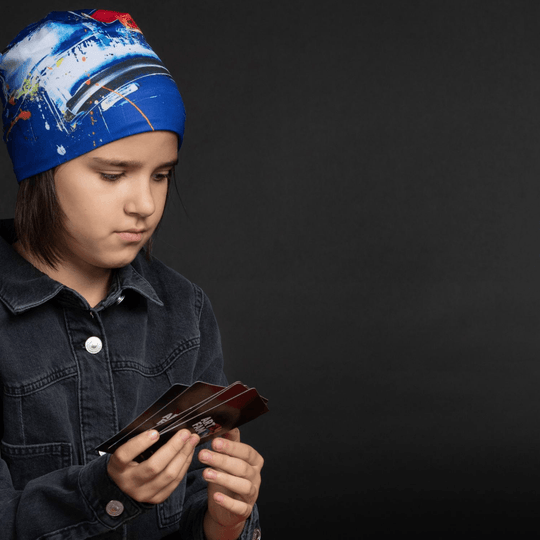 Young person wearing the abstract blue beanie and a denim jacket, looking thoughtfully at a deck of cards.