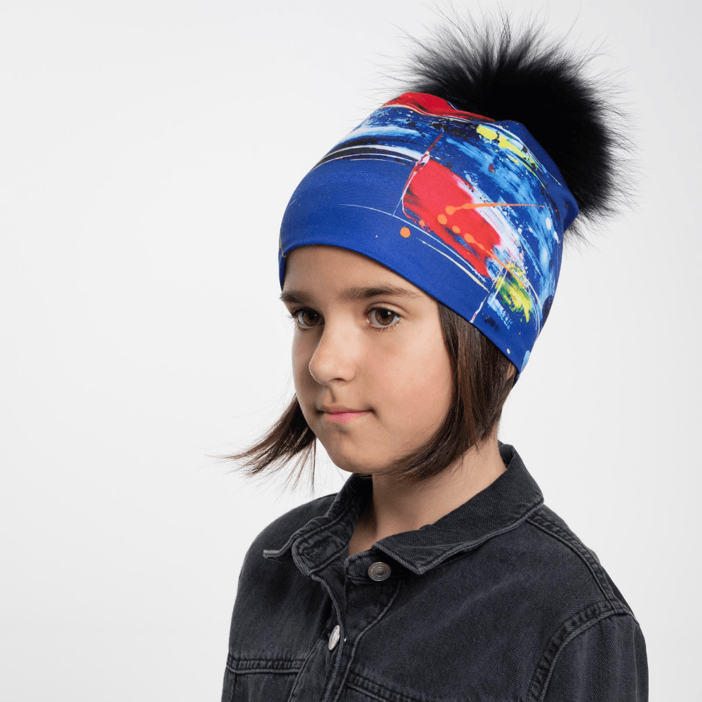 A young girl wearing the Abstract Blue Beanie with a removable black pompom.