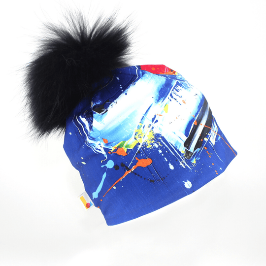 Abstract Blue Beanie with a large black fluffy pompom against a white background.