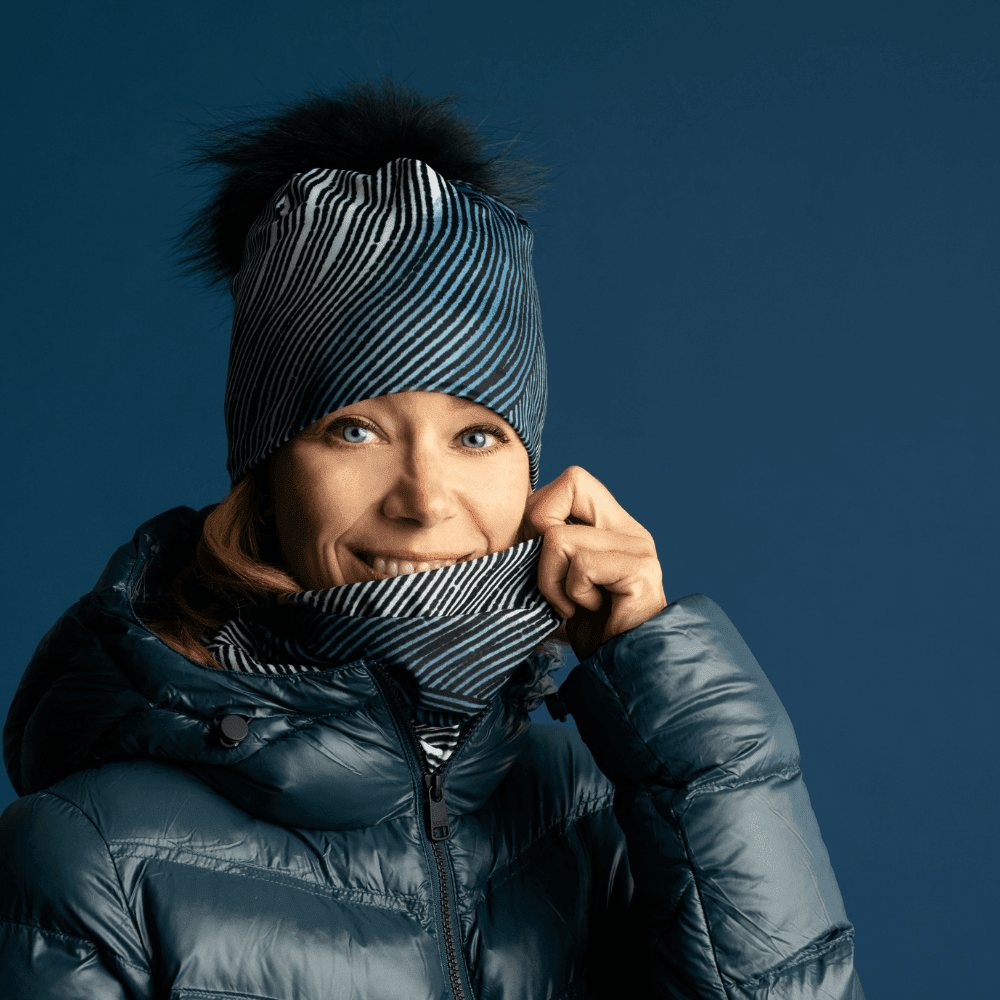 Woman wearing a blue winter jacket, a matching abstract patterned beanie, and neck gaiter pulled up.