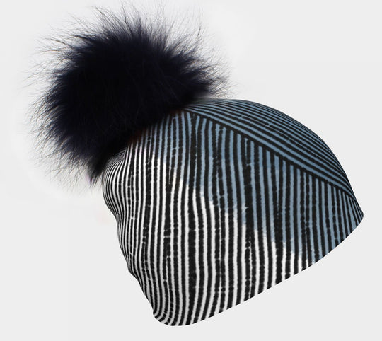 Close-up of a black and white striped beanie with blue accents and a fluffy black pompom on top.