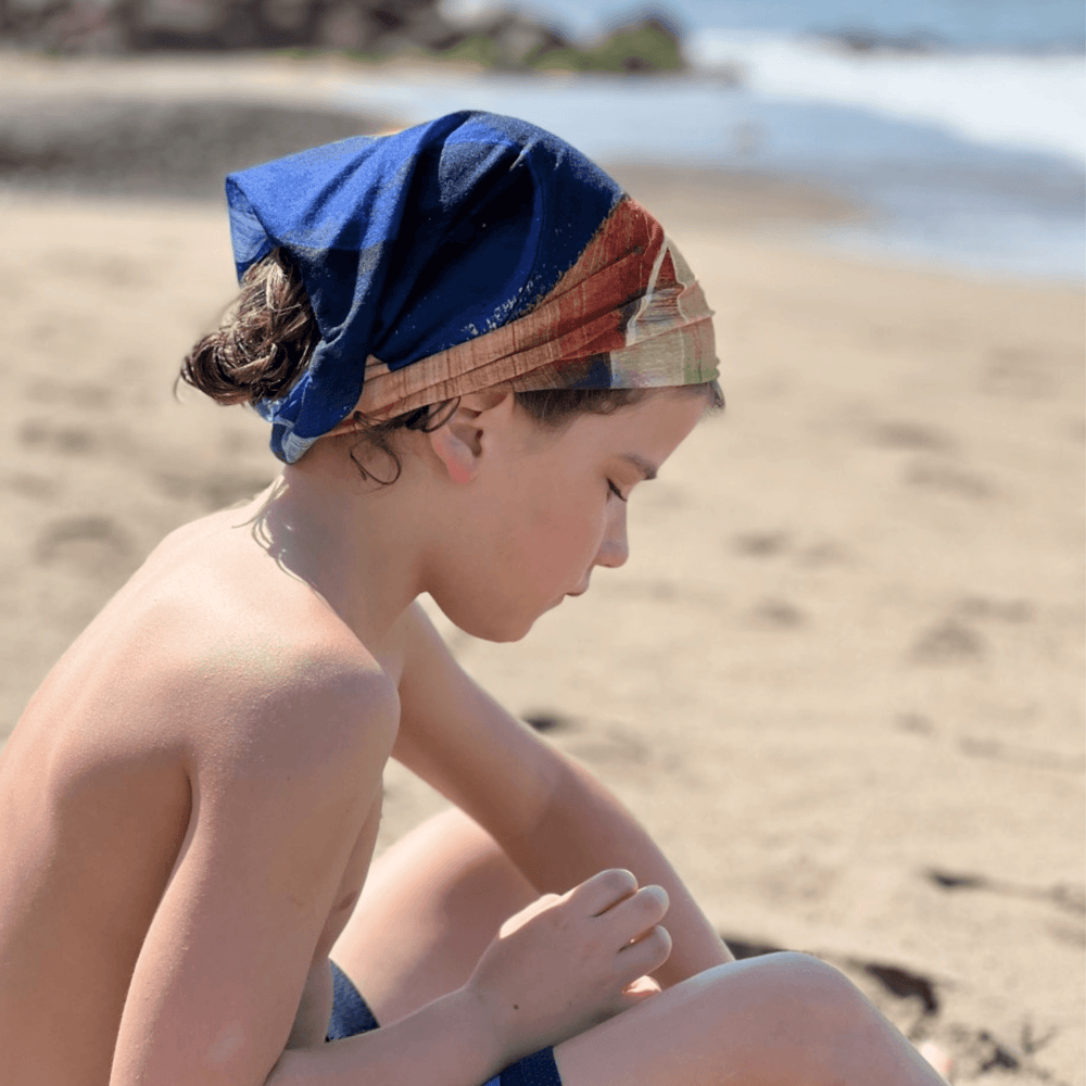 A child on a beach wears the yellow and blue abstract art neck tube as a bandana.
