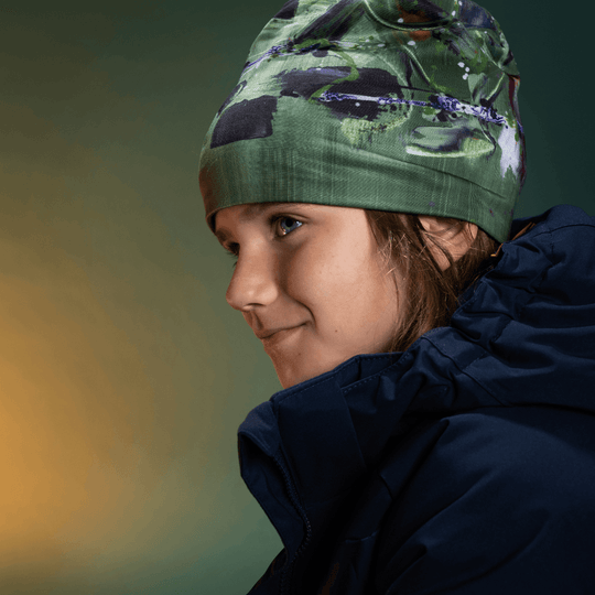 Young person wearing the Amazonia green beanie and a navy blue winter jacket, looking to the side.