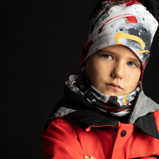 A young boy wearing a colorful abstract beanie and neck gaiter, looking serious.