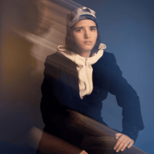 Mannequin portant la tuque Motifs Plumes Bleues, flouté par des traînées de mouvement, sur un dégradé bleu et jaune.