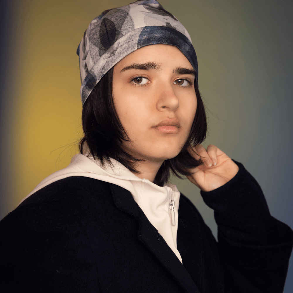 Mannequin portant la tuque Motifs Plumes Bleues avec un sweat à capuche blanc et une veste noire sur fond coloré.