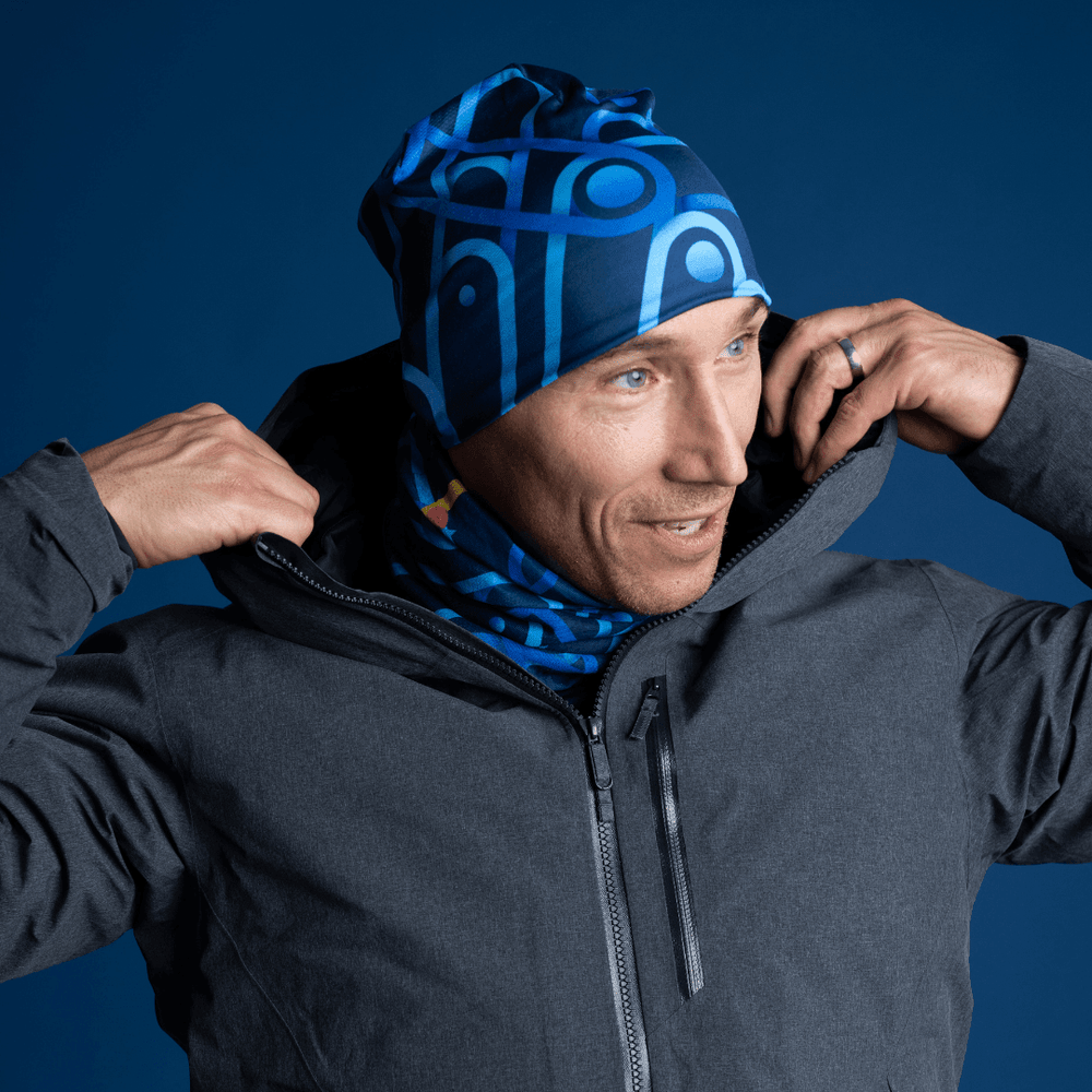 Man wearing a dark grey jacket and a matching blue patterned beanie and neck gaiter.