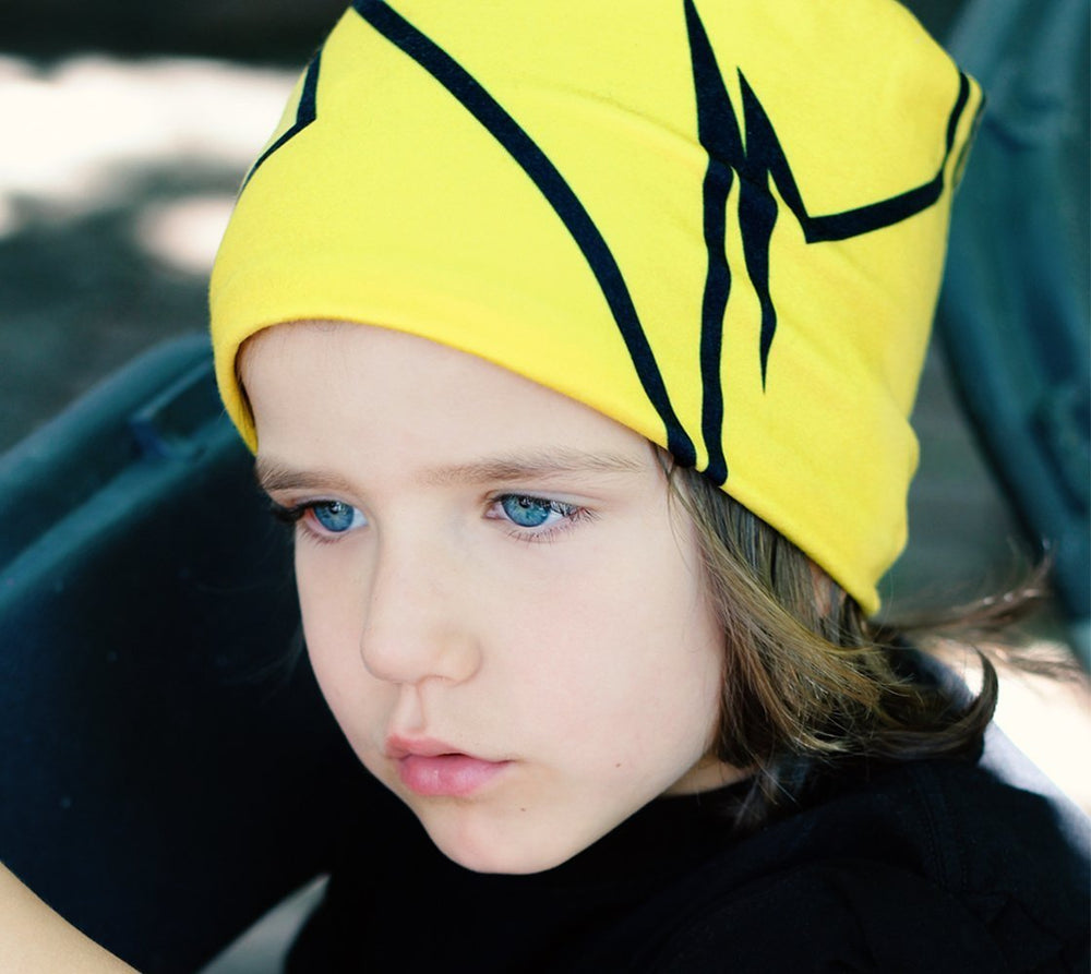 Child with bright blue eyes wearing a yellow beanie with a black broken line pattern.