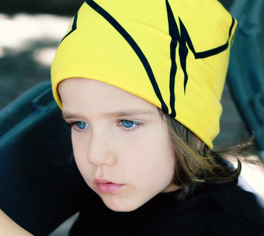 Child with bright blue eyes wearing a yellow beanie with a black broken line pattern.