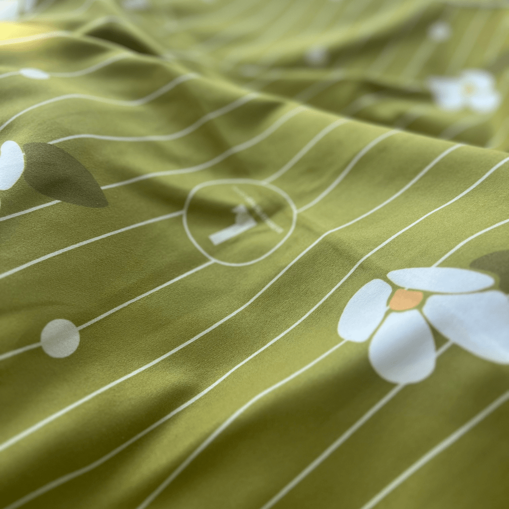Close-up of the soft green reverse side of the Chrysalide towel, showing a subtle pattern of white flowers and stripes.