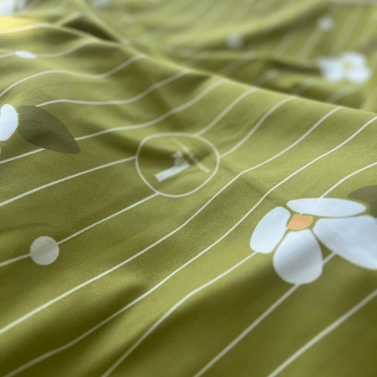 Close-up of the soft green reverse side of the Chrysalide towel, showing a subtle pattern of white flowers and stripes.