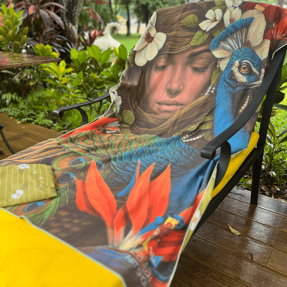 The Chrysalide artistic beach towel draped over an outdoor chair, showcasing its colorful artwork and included pouch.