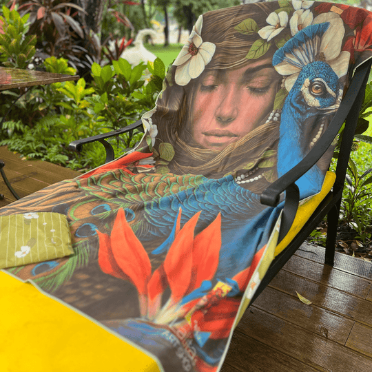 The Chrysalide artistic beach towel draped over an outdoor chair, showcasing its colorful artwork and included pouch.