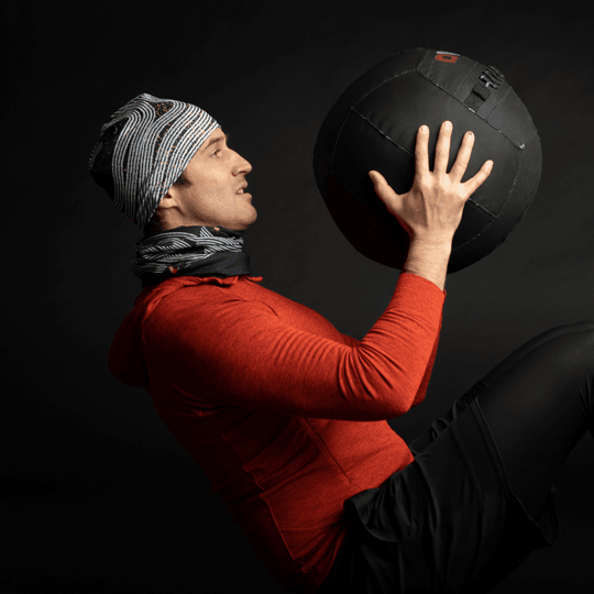 Man in red hoodie and black shorts wearing the Dark Steel Multifunctional Tube as a neck warmer while holding a medicine ball