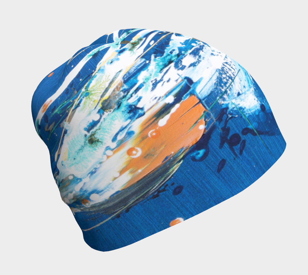 A blue beanie with abstract earth-toned splatters and brushstrokes, shown from the side.