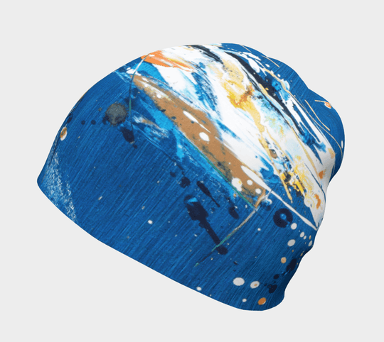 A blue beanie with abstract earth-toned splatters and brushstrokes, shown from the side.