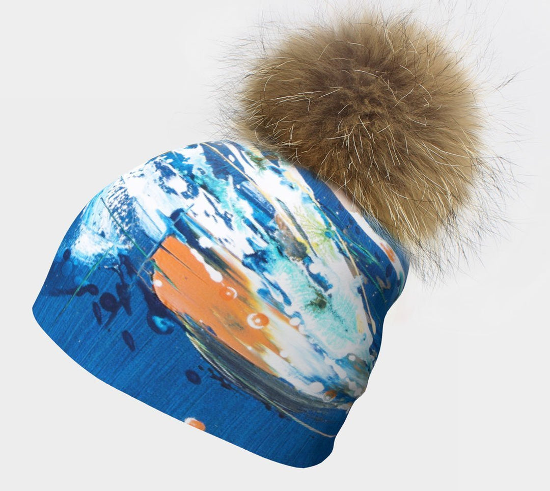 Close-up of the blue abstract art beanie with a fluffy pompom, on a white background.