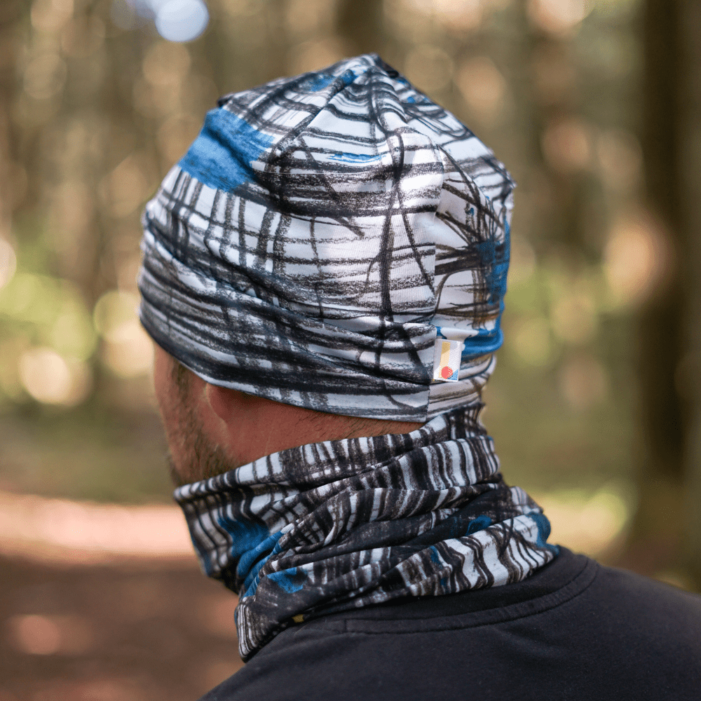 A man wearing the Expressive Sketch Beanie and matching neck tube outdoors in a forest setting.