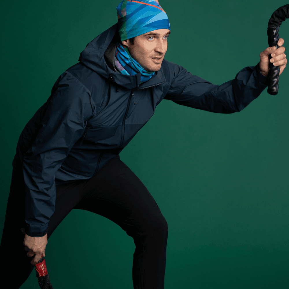 Man wearing a dark jacket and the abstract pattern neck tube and matching beanie, holding workout ropes.