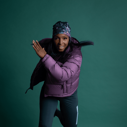 Woman in a purple puffer jacket and floral beanie captured mid-stride, looking energetic.