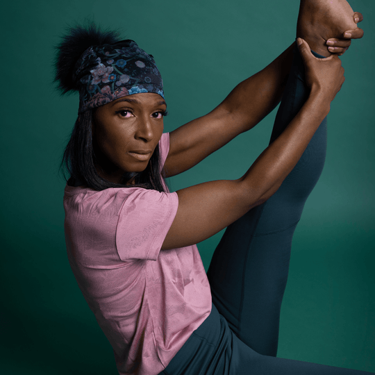Close-up of a woman performing a difficult yoga pose, wearing the Flora Pompom Beanie.