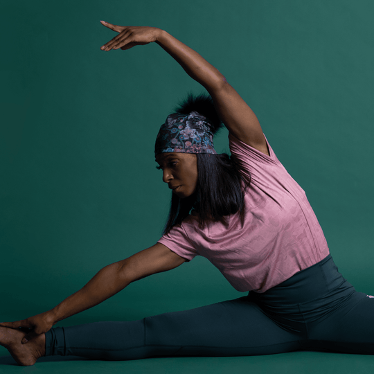 Woman in a pink top and dark leggings performing a yoga pose, wearing the Flora Pompom Beanie.