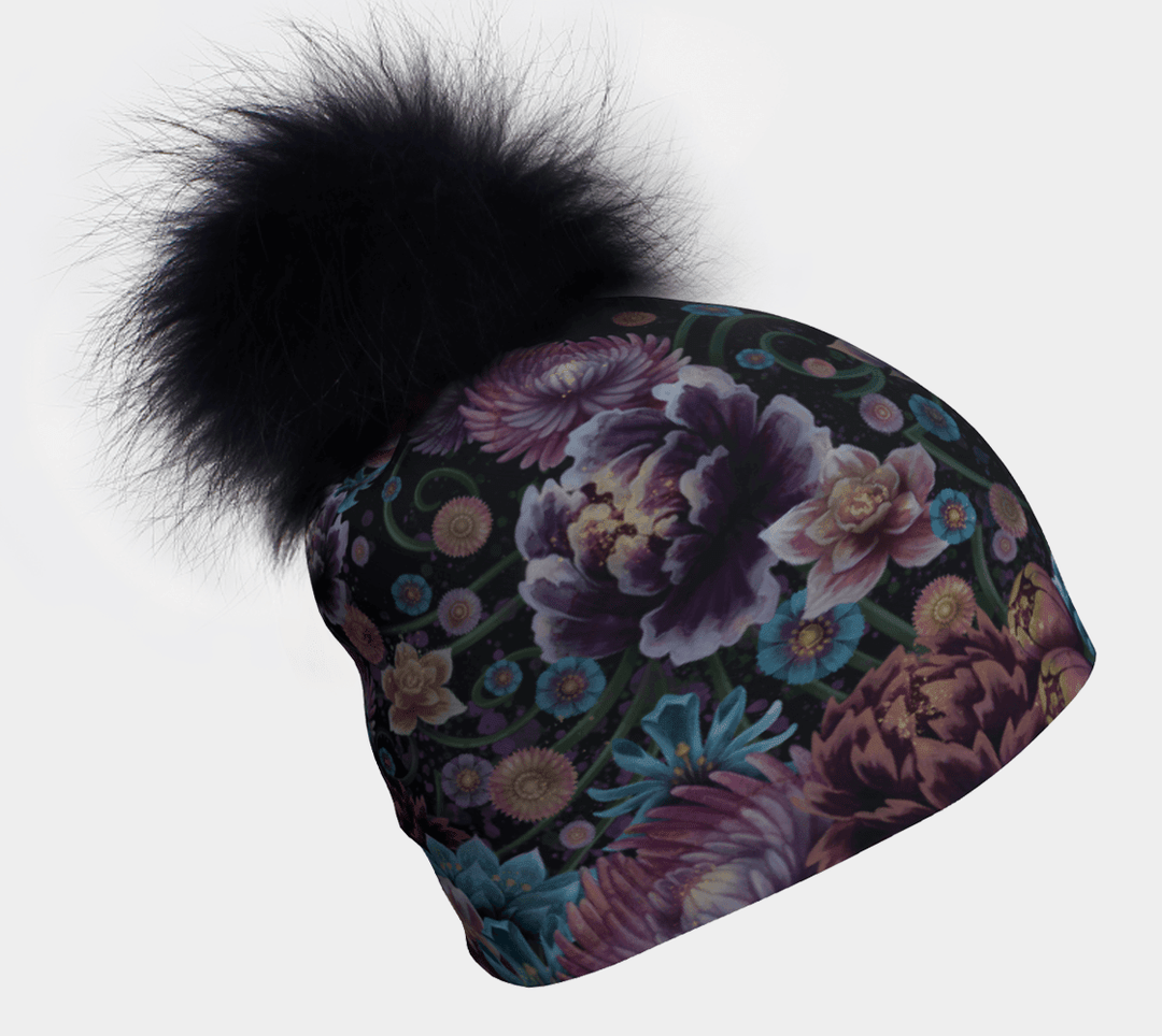 Flora Pompom Beanie with a large black fluffy pompom and a vibrant floral pattern on a dark background, shown from the side.