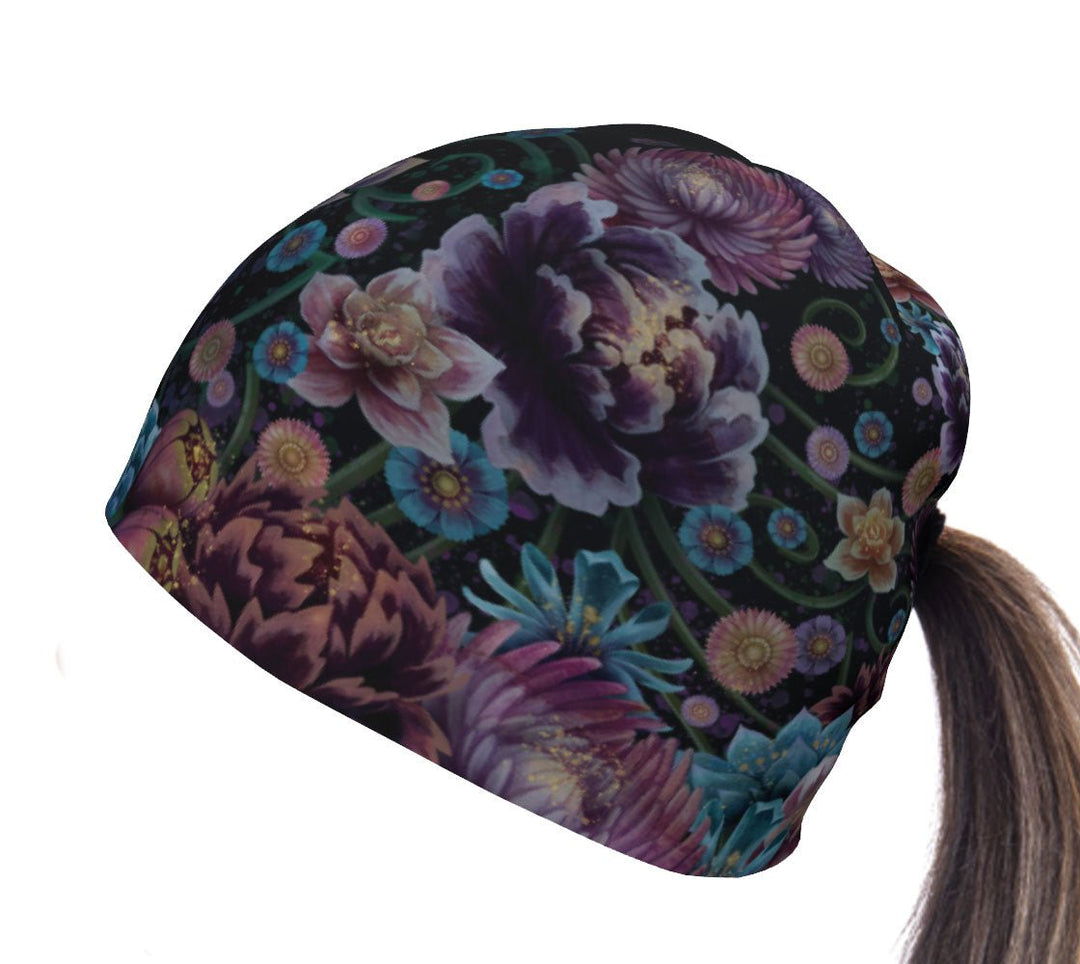 Close-up of a black beanie with a vibrant, dark floral pattern featuring purple, blue, and pink blooms, designed for a ponytail.