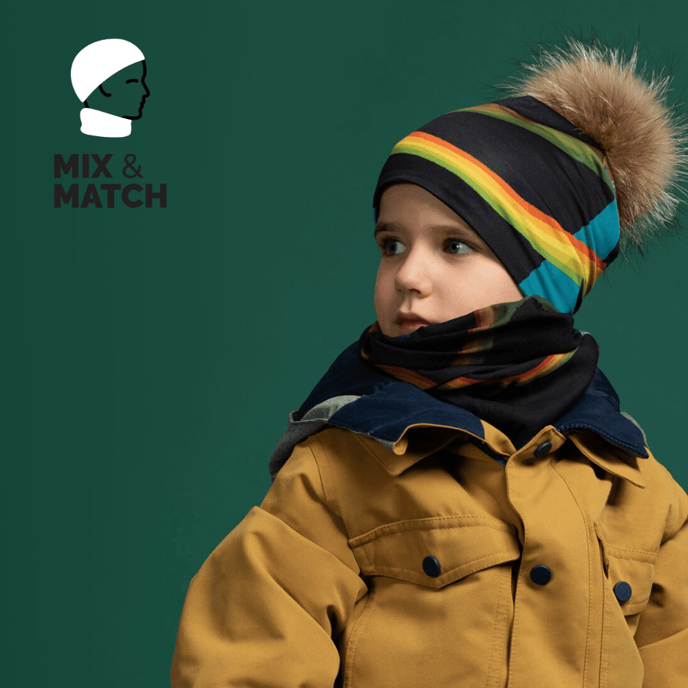 Young boy wearing a yellow jacket and a colourful striped beanie with a detachable fur pompom, with a matching neck gaiter.