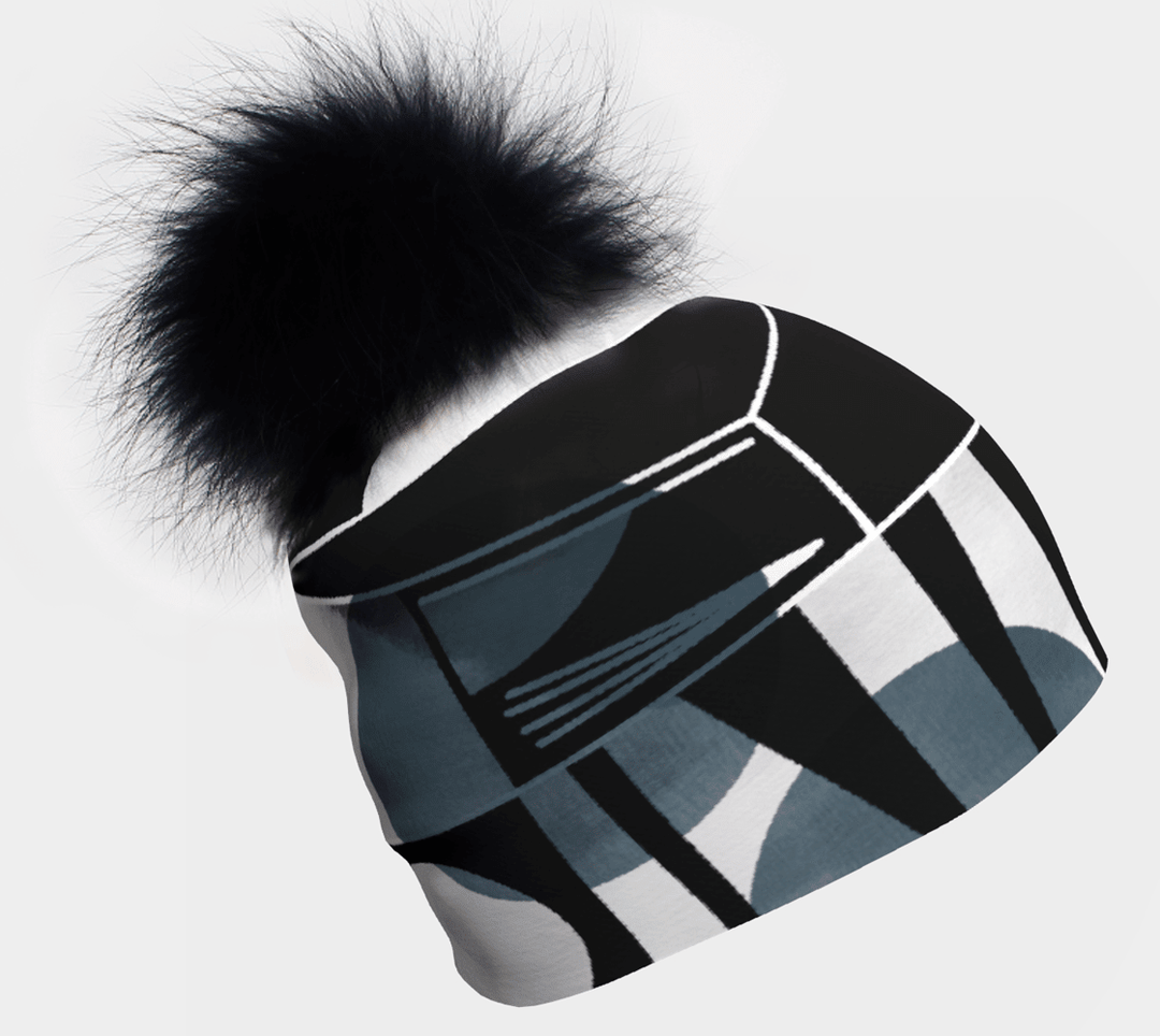 Close-up of a black and grey geometric print beanie with a large black pompom against a white background.