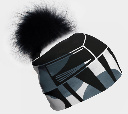 Close-up of a black and grey geometric print beanie with a large black pompom against a white background.
