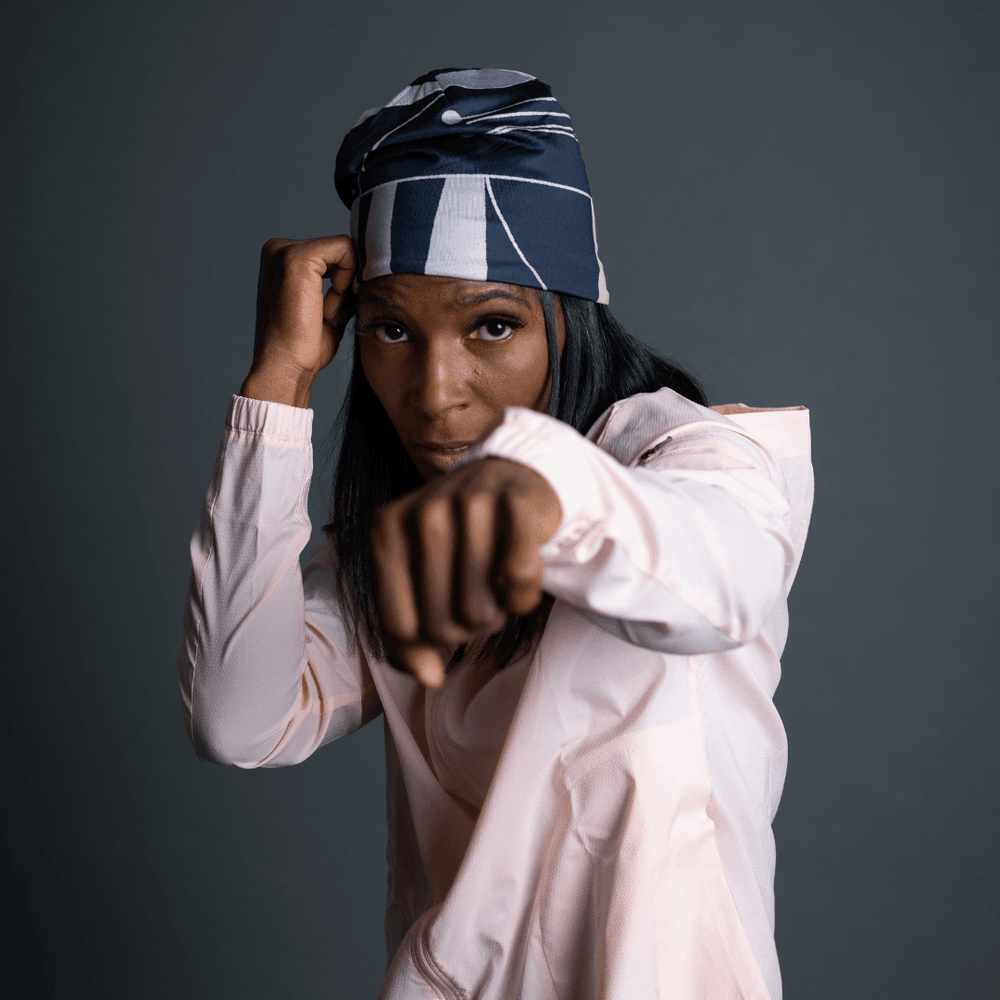 A woman wearing a black and blue striped beanie and a light pink windbreaker, in a boxing stance.