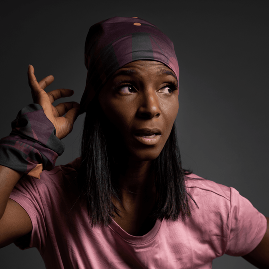A woman in a pink t-shirt adjusts the purple geometric patterned bandana on her head, looking off to the side.