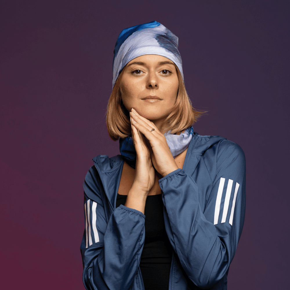 Woman looking thoughtfully at the camera, wearing the Golden Sea Beanie and neck tube, hands clasped at chin.