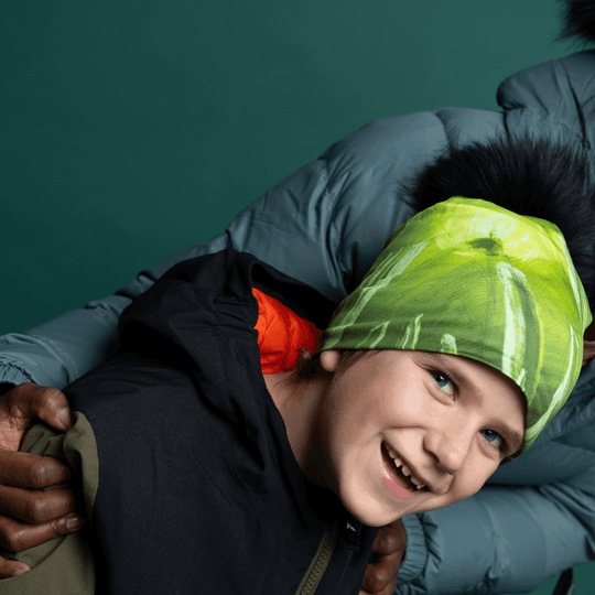 Two people embracing, with one wearing the Green Light Thin Beanie featuring a green art print and black pompom.
