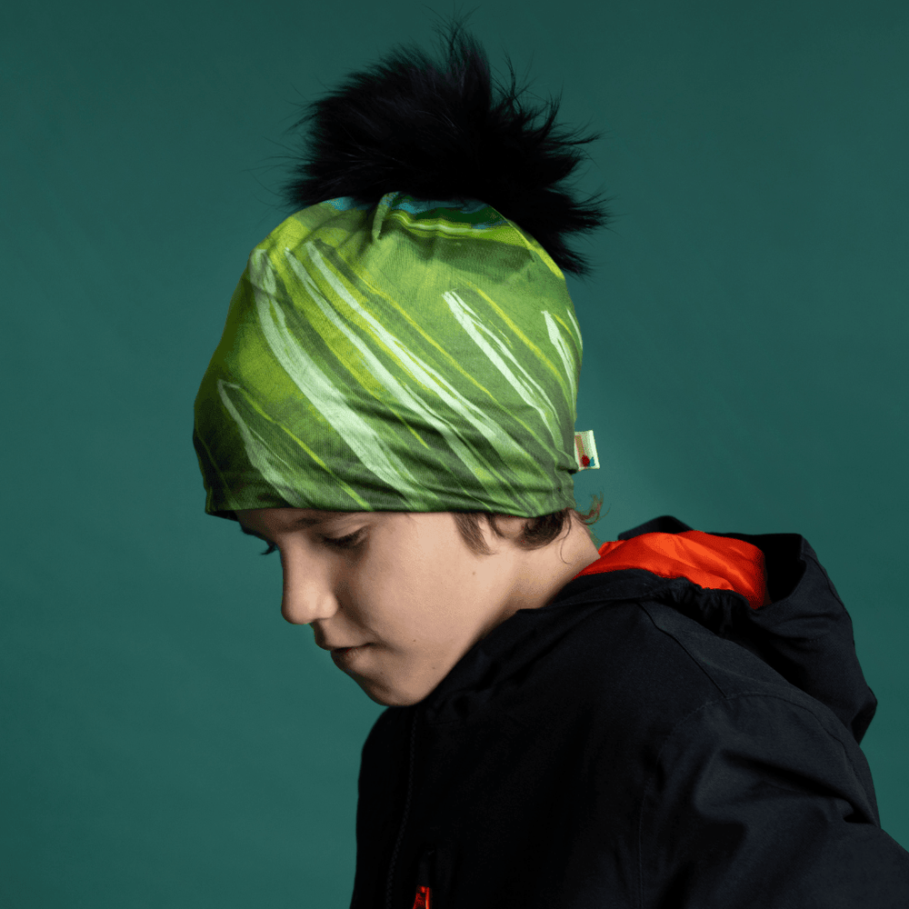 Young boy wearing the Green Light Thin Beanie with a black pompom, looking to the side.