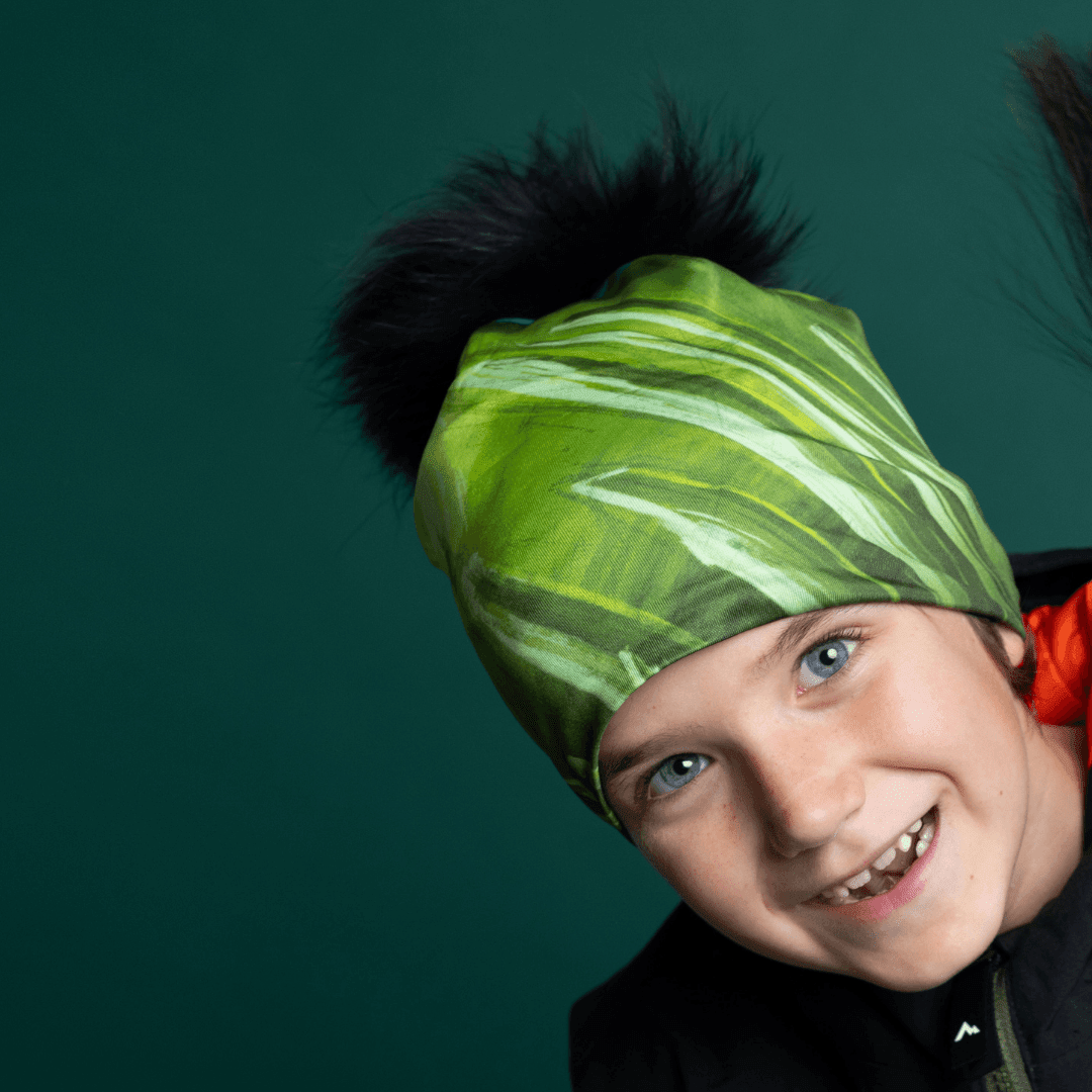 Close-up of a smiling child wearing the Green Light Thin Beanie with a black pompom.