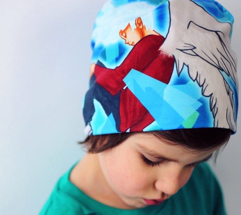 A young child wearing the "Head In The Clouds" beanie, which features a blue and abstract art design with an angelic figure.