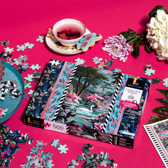 Jigsaw Puzzle "Flying High" box surrounded by scattered puzzle pieces and a cup of tea.