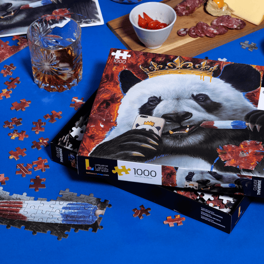 A partially assembled Selfie Panda 1000-piece jigsaw puzzle on a blue surface, surrounded by scattered pieces and a drink.