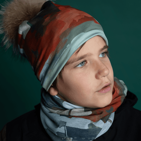 A young person wears a matching Lachine beanie and multifunctional tube, looking thoughtfully to the side against a dark teal background.