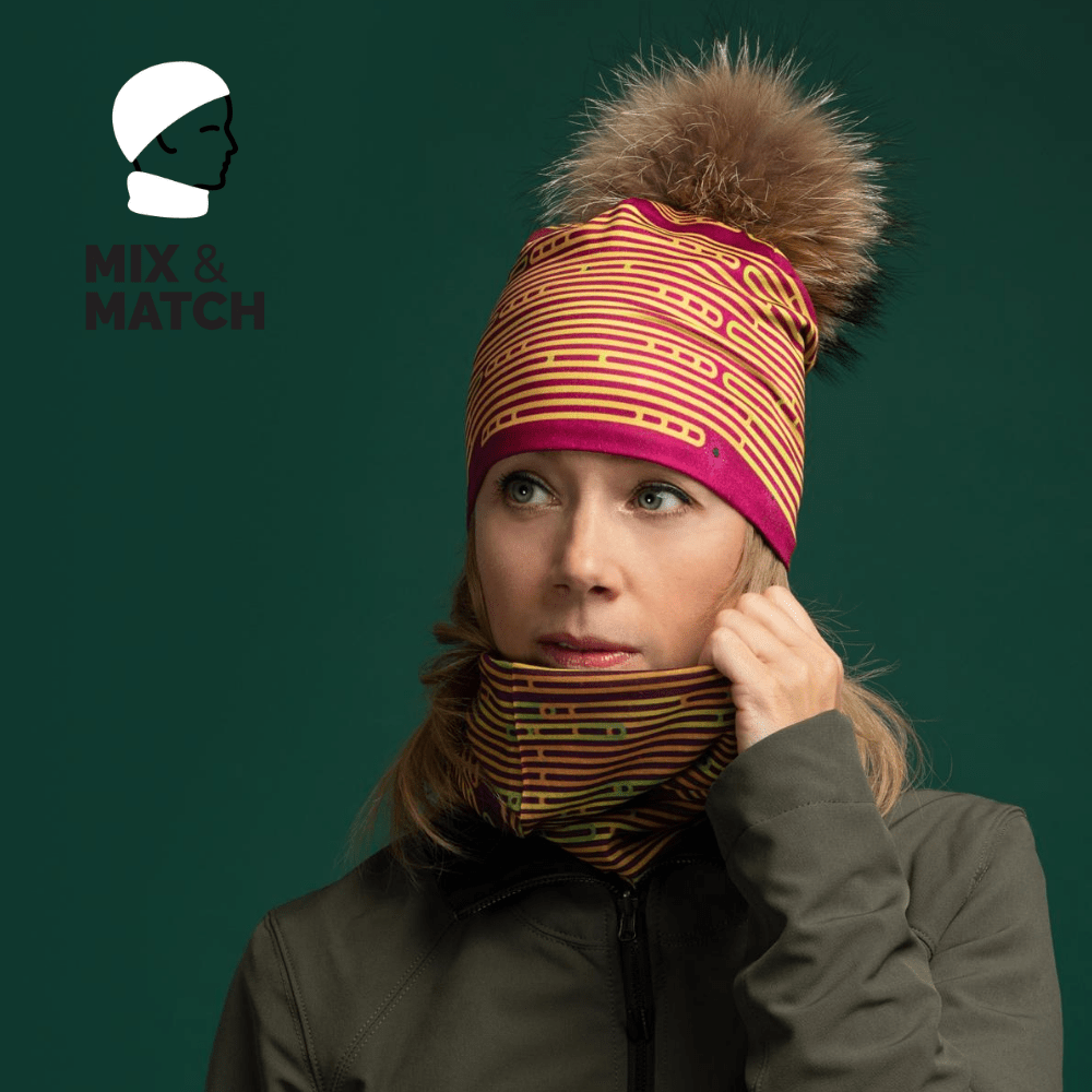 Woman wearing a matching magenta and yellow striped beanie and neck gaiter, styled with a green jacket against a dark green background.