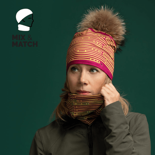Woman wearing a matching magenta and yellow striped beanie and neck gaiter, styled with a green jacket against a dark green background.