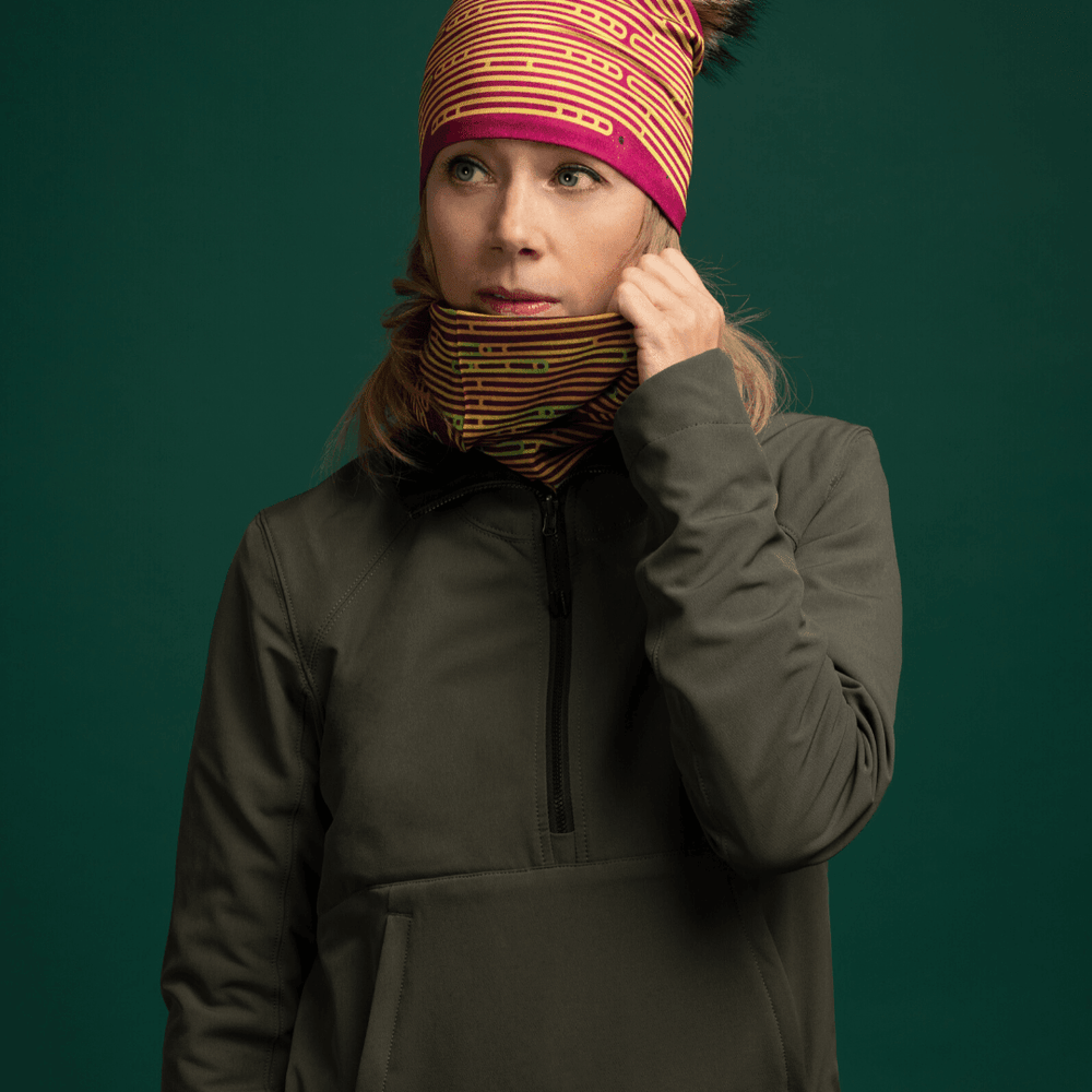 Woman wearing a dark green jacket, adjusting a Magenta Multifunctional Tube around her neck, which features a colourful abstract stripe pattern.