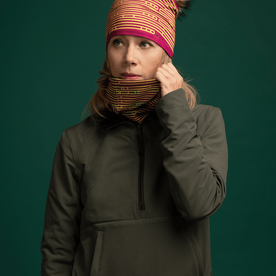 Woman wearing a dark green jacket, adjusting a Magenta Multifunctional Tube around her neck, which features a colourful abstract stripe pattern.