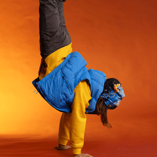 A person in a blue vest and yellow hoodie performing a handstand, wearing the MatriX Beanie.