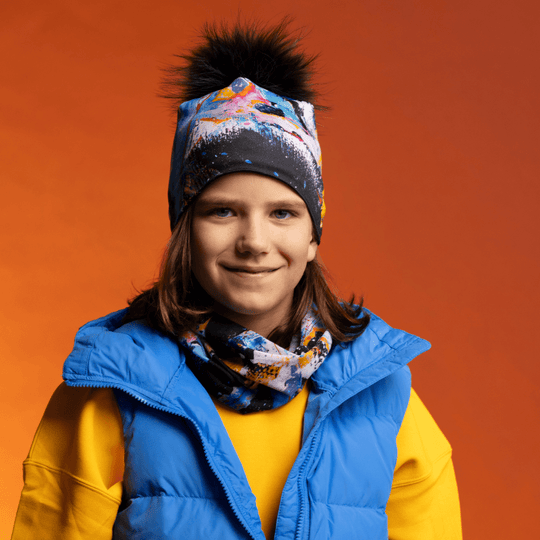 A smiling young person wearing the MatriX Beanie and matching neck tube, layered under a blue vest and yellow shirt.